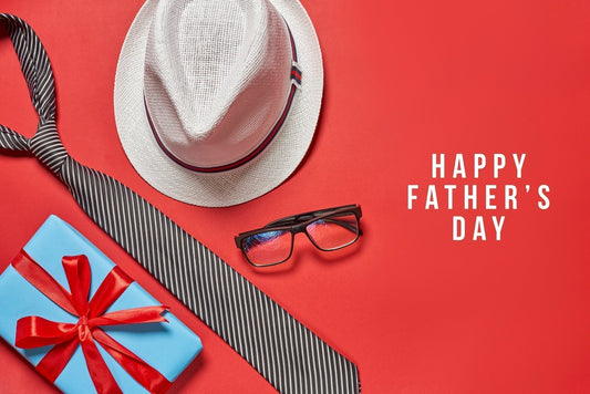 Flat lay of Father's Day items on a red background, including a white fedora hat, striped necktie, eyeglasses, and a blue gift box with a red ribbon, alongside the text 'Happy Father's Day'.